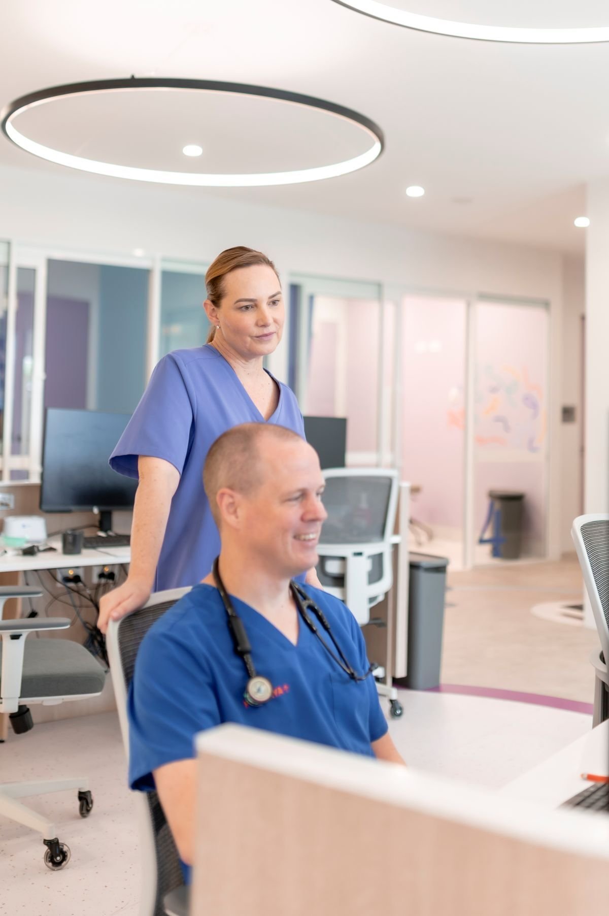 Doctor and Nurse Smiling in Staff Work Area with Consult Rooms Behind